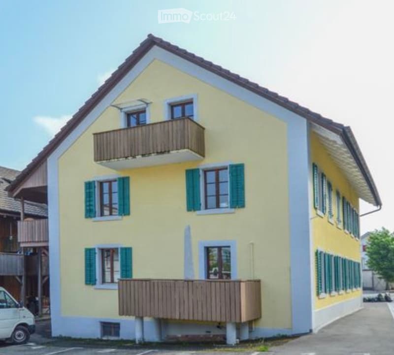 House. Two-story yellow house with green shutters, multiple windows, and two balconies on the upper floor.