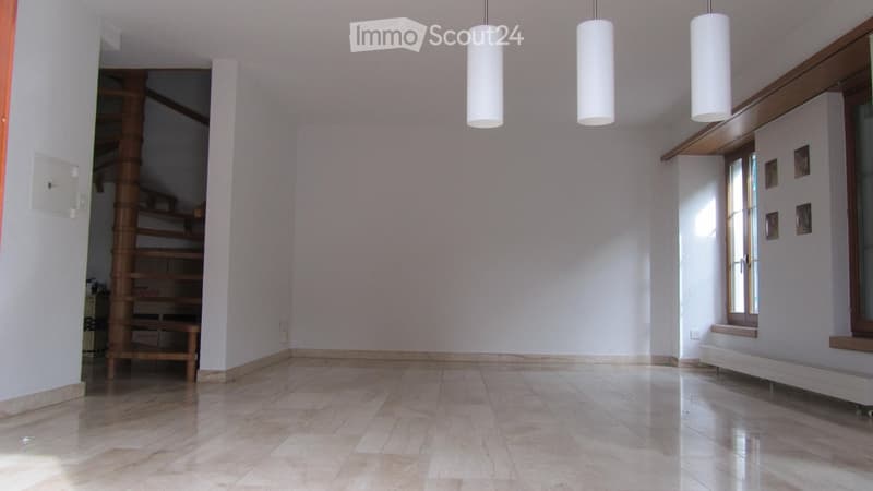 Corridor / Hallway. Empty hallway with tiled floor, white walls, and a spiral staircase leading upwards. Three pendant lights hang from the ceiling, and there is a window on the right side.