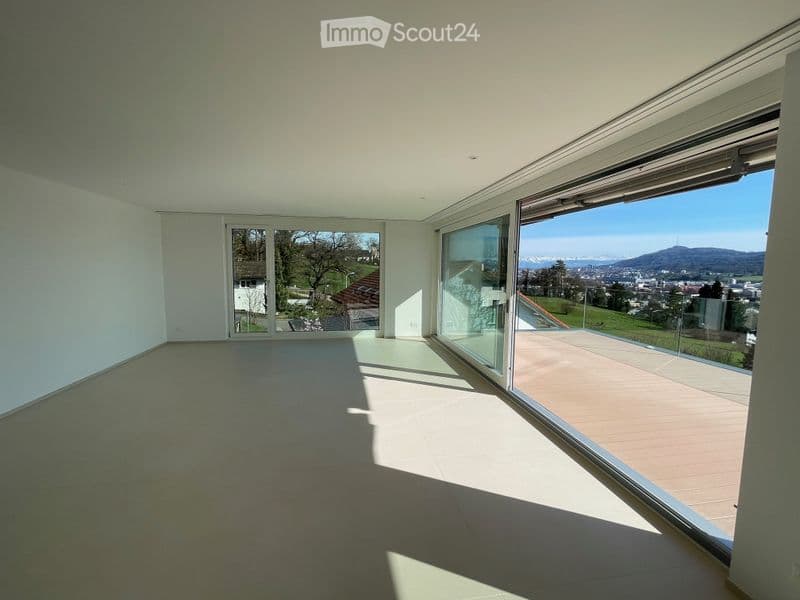 Empty room with large glass sliding doors leading to a balcony, offering a scenic view of the landscape and city.