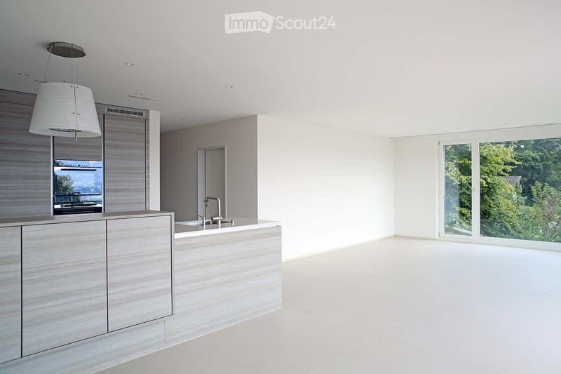Modern kitchen with a grey kitchen island, sleek faucet, and pendant light. Large windows offer a view of greenery outside.