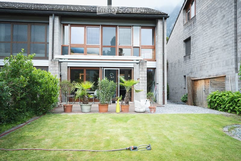 Well-maintained garden with a lawn, potted plants, and a modern house in the background.