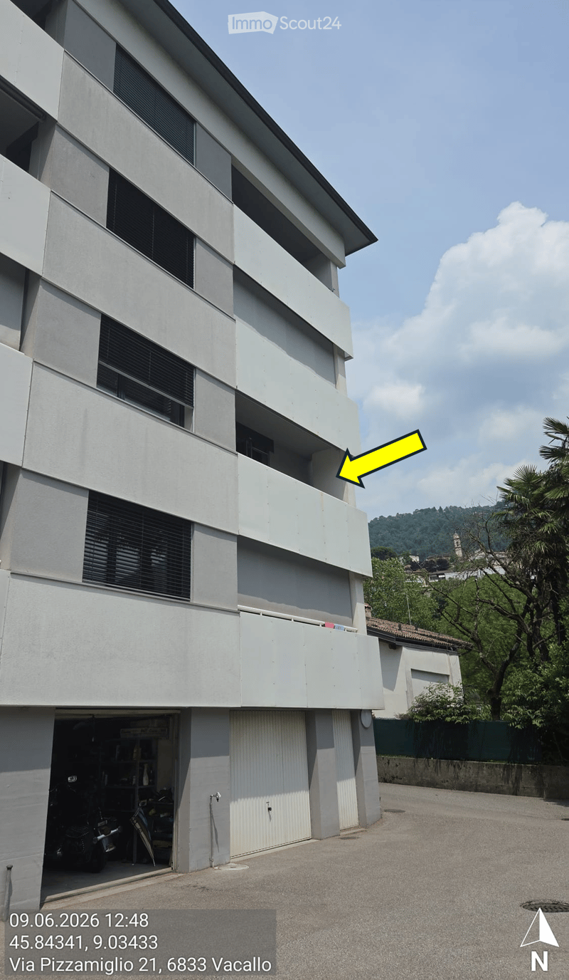 Modern multi-story building with white facade, large windows, and balconies. Garage visible at the bottom left.