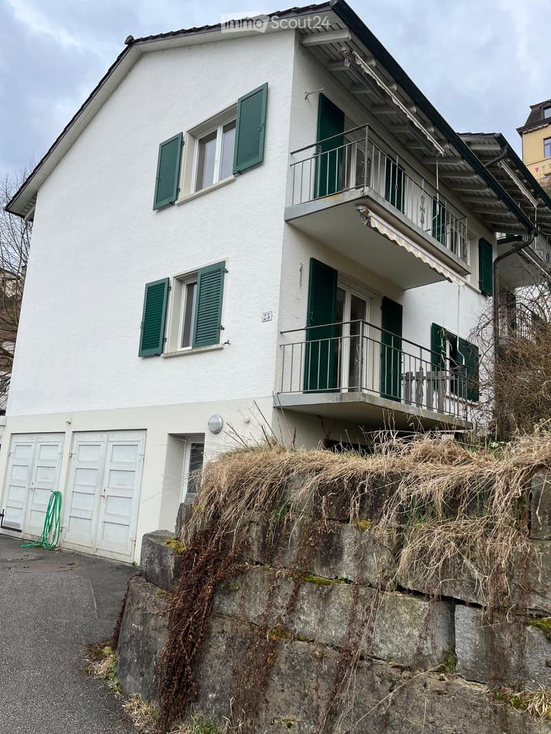 Two-story white house with green shutters, balcony, and garage.