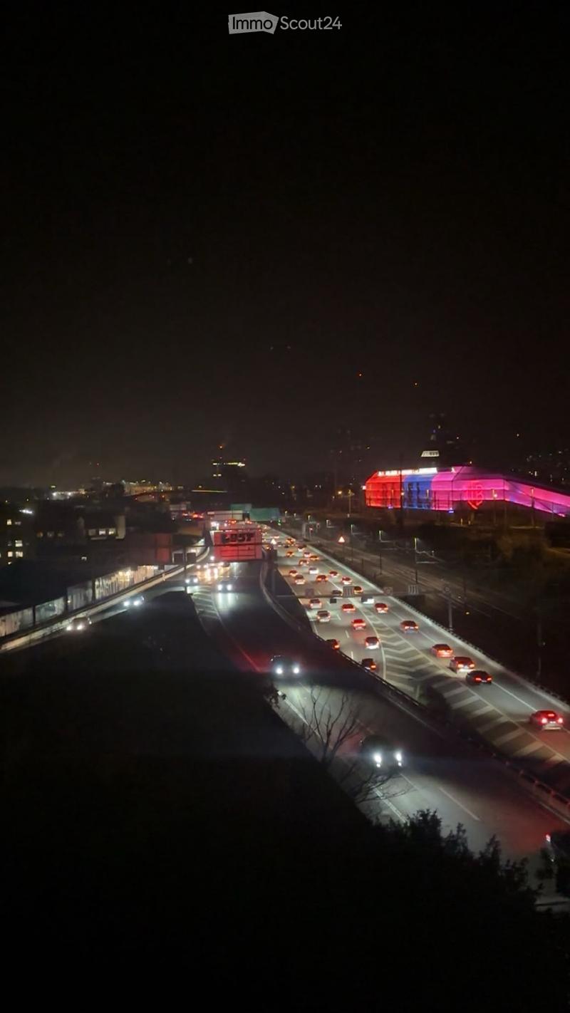Nighttime aerial view of a busy highway with multiple lanes of traffic, illuminated vehicles, and distant city lights.
