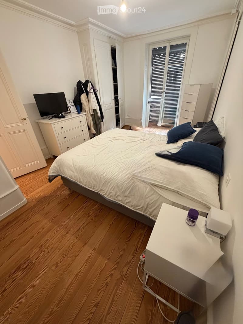Cozy bedroom with wooden flooring, a neatly made bed with pillows, a nightstand, a drawer unit, and a screen on a small table.