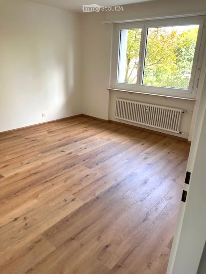 Empty room with wooden flooring, white walls, and a window with a radiator below it.