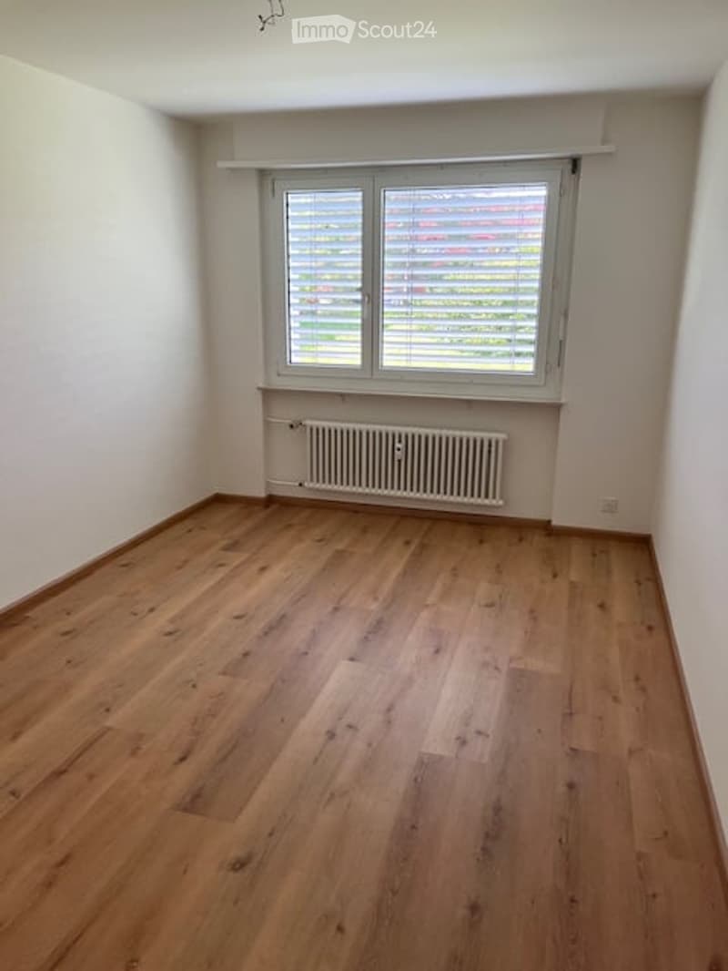 Empty room with wooden flooring, white walls, a window with blinds, and a radiator below the window.