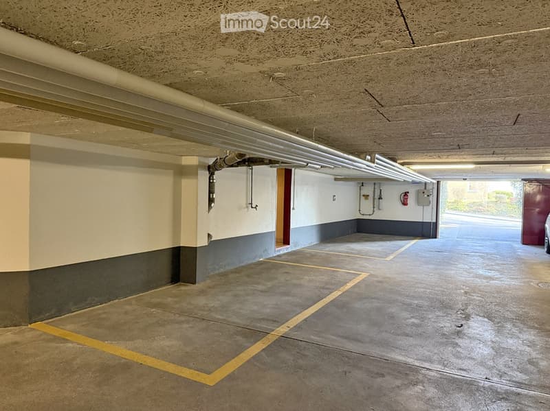 Underground parking garage with concrete floors, white walls, and yellow parking lines.