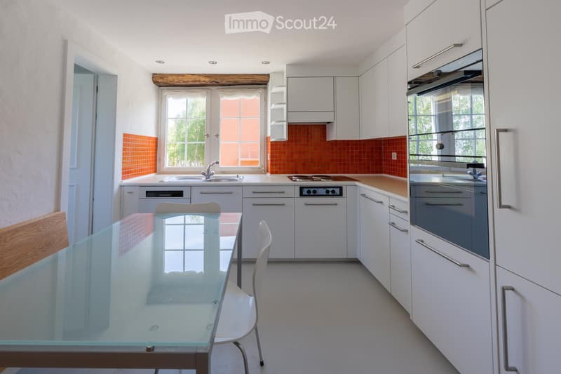 Modern kitchen with white cabinets, stainless steel appliances, a glass dining table, and a white chair.