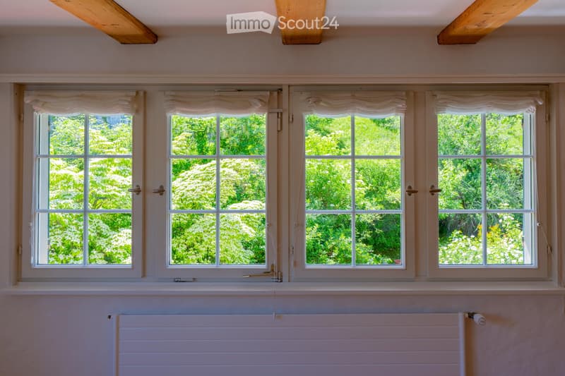 Empty room with four large windows, white radiator, and light-colored walls.