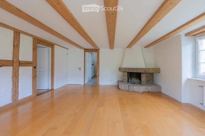 Empty room with wooden beams, polished wooden floor, fireplace, and white walls.