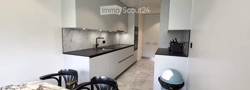 Modern kitchen with white cabinets, black countertops, a sink, and a small dining area with chairs and a table.
