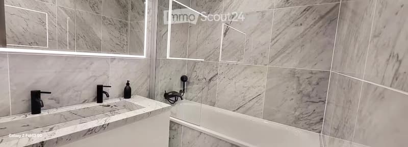 Modern bathroom with marble tiles, double sink, bathtub, and large mirror.