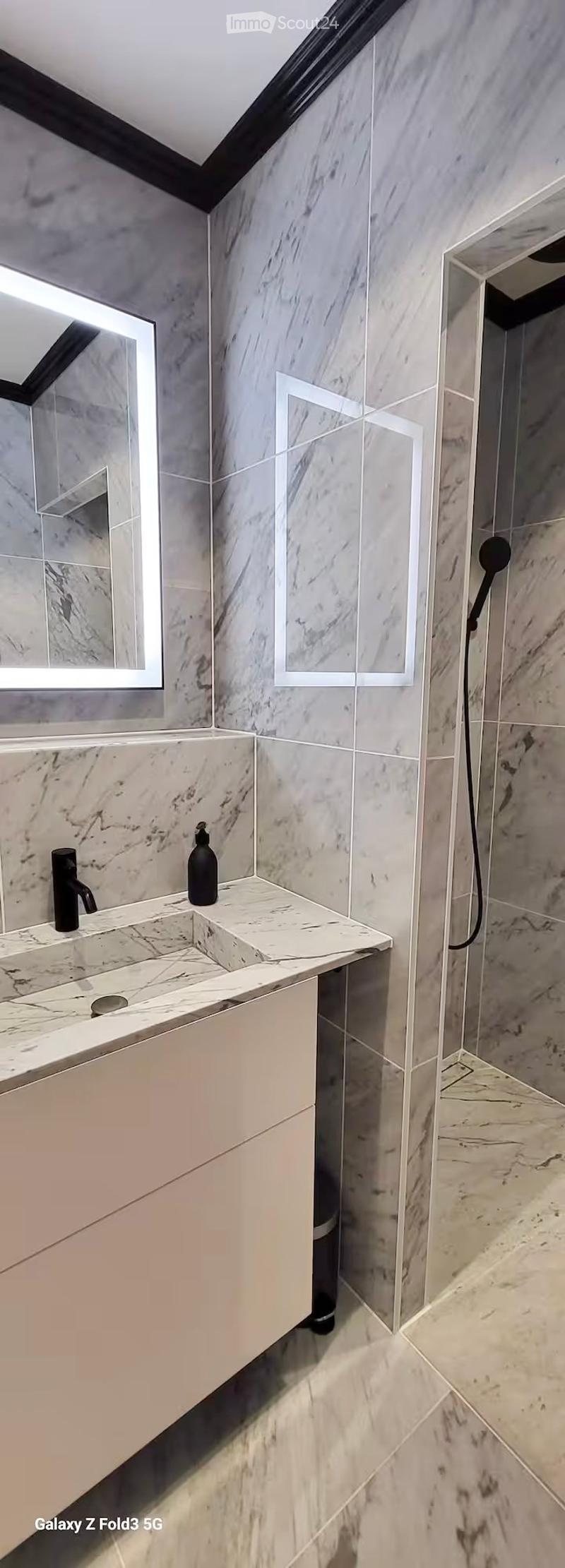 Modern bathroom with marble tiles, a sleek sink with a black faucet, a large mirror, and a shower area with a handheld showerhead.