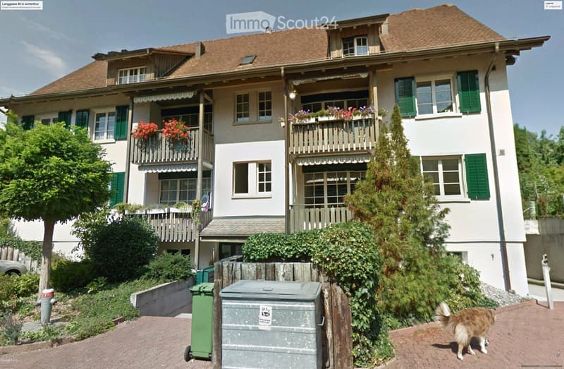 2 story house, brown roof, green shutters, balconies, garden, trash bins