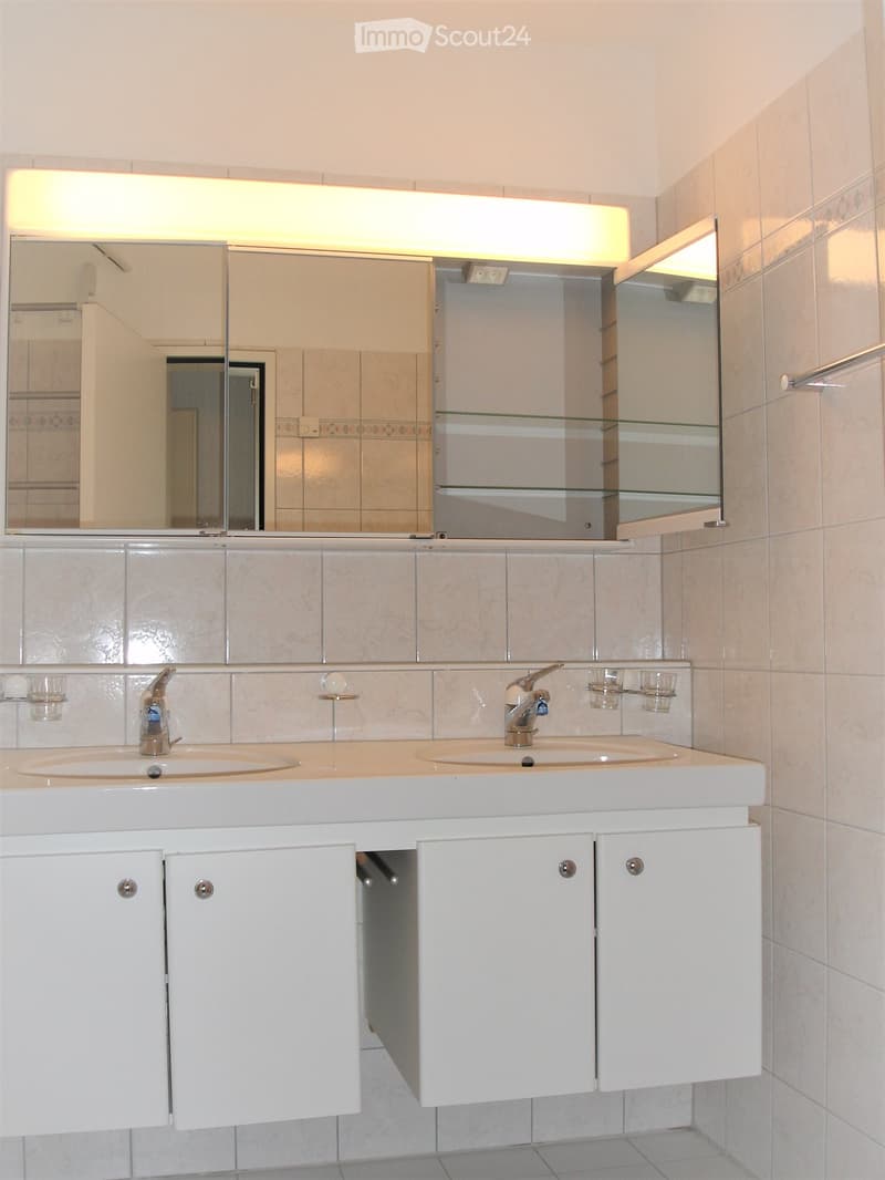 modern bathroom with double sink, mirror, cabinets, and tiled walls