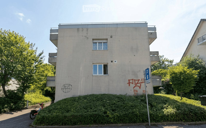 Four-story residential building with balconies, graffiti on the facade, and a parking sign nearby.