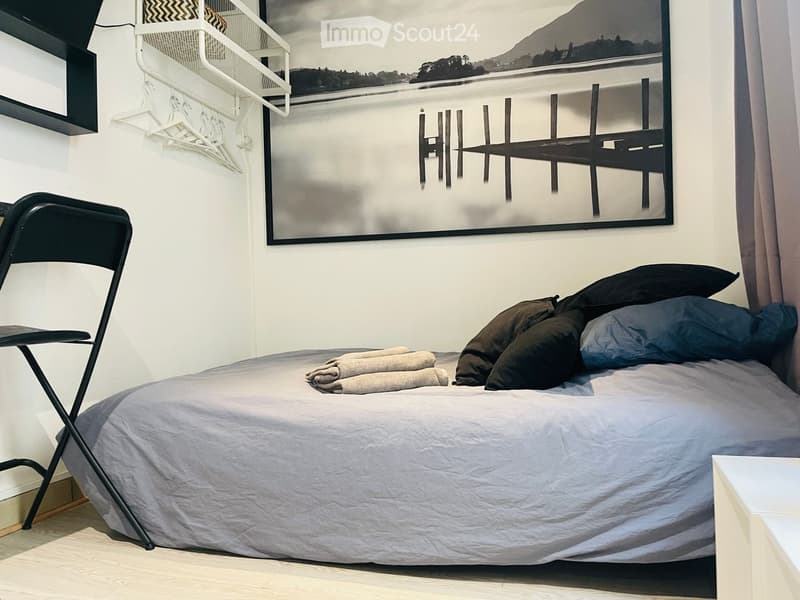Cozy bedroom with a single bed, folded towels, a chair, and a large picture frame on the wall.