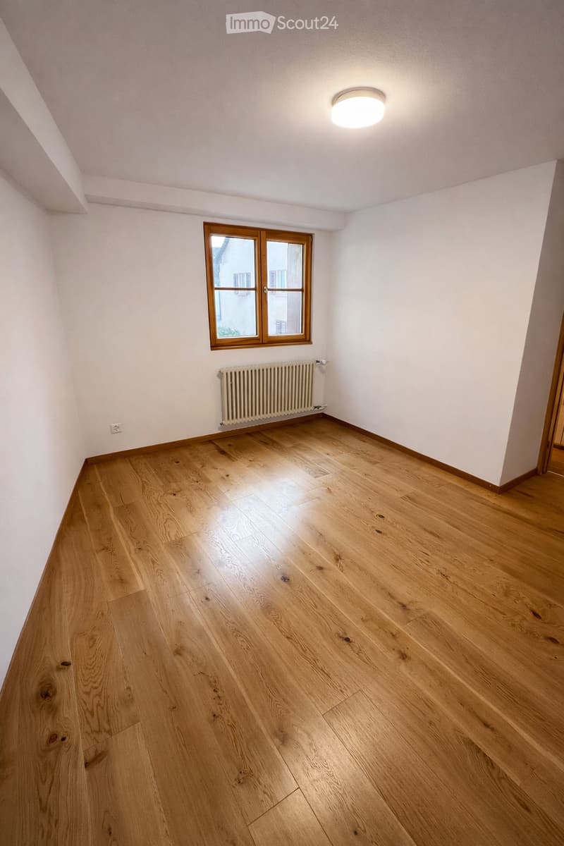empty room with wooden floor, white walls, central heating, window with a view