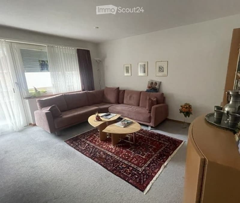 Living room with a large window, a pink sectional sofa, a wooden coffee table, a patterned rug, and decorative picture frames on the wall.