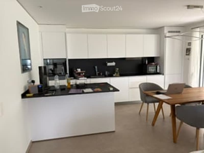 Modern kitchen with white cabinets, black countertops, and a central island. Includes a dining area with a table and chairs, and a laptop on the table.