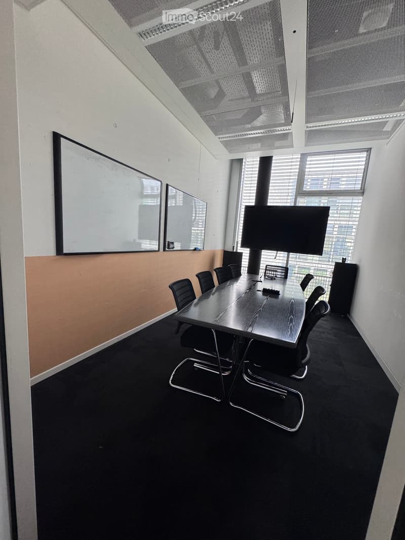 Conference room with a long wooden table, black chairs, a large screen, and mirrors on the wall.