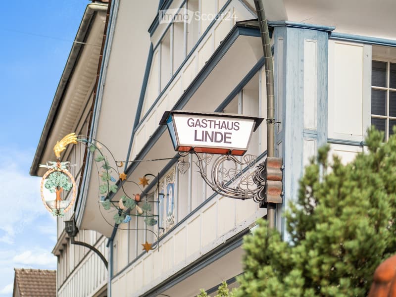 Facade of a traditional building with a sign reading "GASTHAUS LINDE" and decorative wrought iron elements.