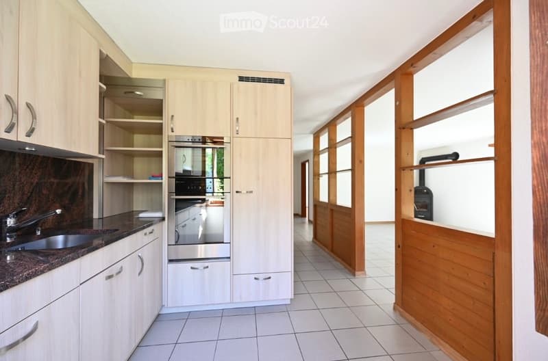 Modern kitchen with light wood cabinets, stainless steel oven, granite countertop, and tiled floor.