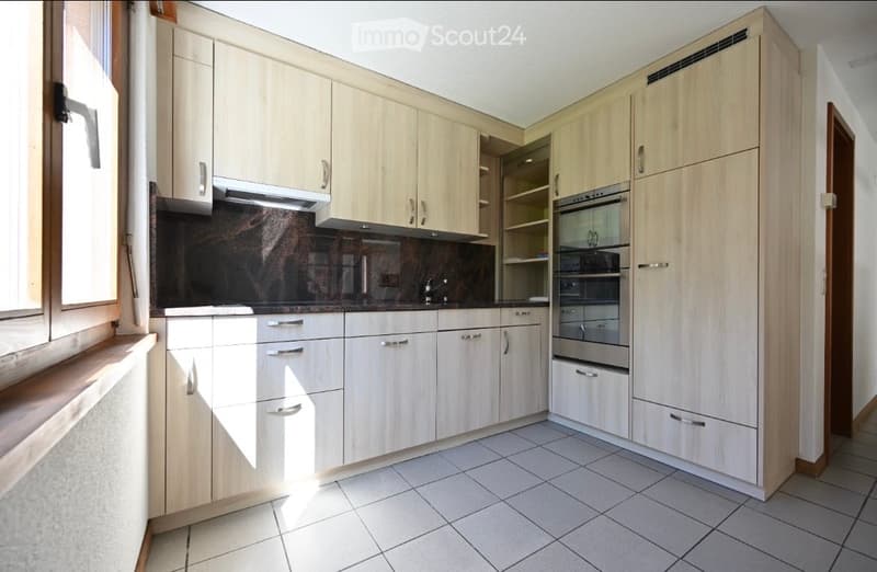 Modern kitchen with light wood cabinets, stainless steel oven, and tiled floor.