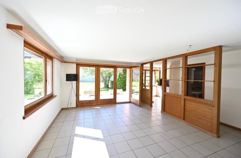 Empty room with tiled floor, white walls, large windows, and wooden sliding doors leading to an outdoor area.