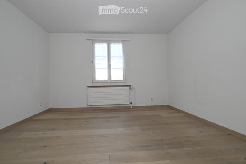 Empty room with wooden flooring, white walls, and a window with a radiator below it.