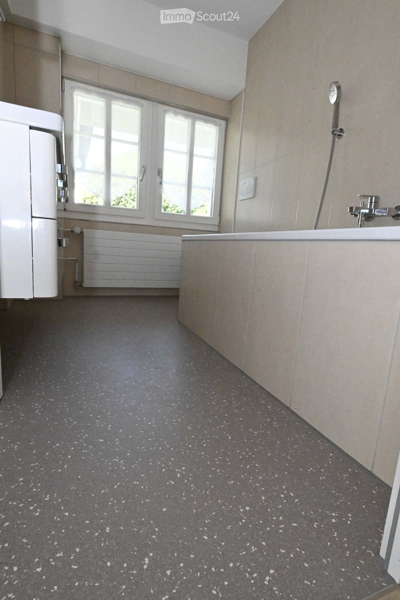 Modern bathroom with a bathtub, faucet, radiator, and cabinet. The floor features a speckled grey design.
