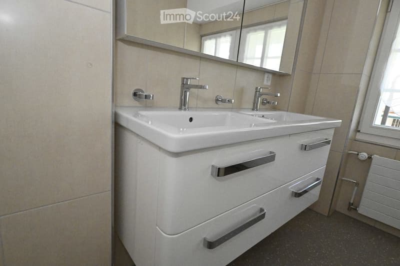 Modern bathroom with a double sink, sleek chrome faucets, a large mirror, and a white cabinet with multiple drawers and handles.