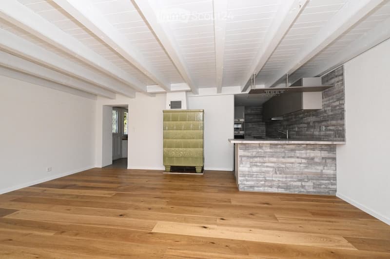 Open-concept space with wooden flooring, white walls, and a kitchen area featuring a stone island and modern appliances.