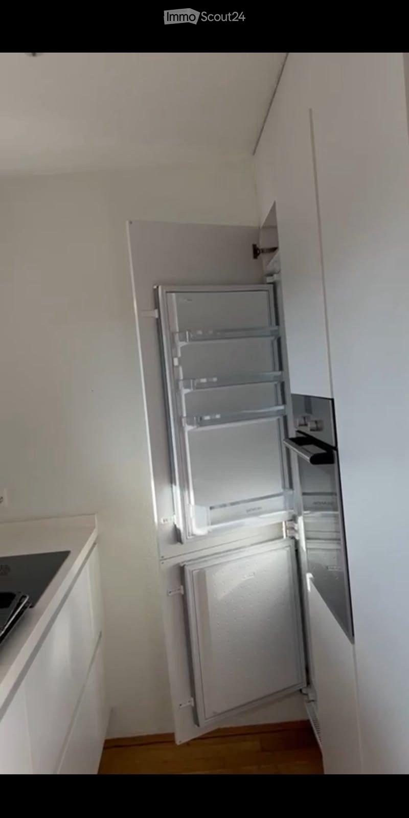 A compact kitchen with a stainless steel refrigerator, white cabinets, and a wooden floor.