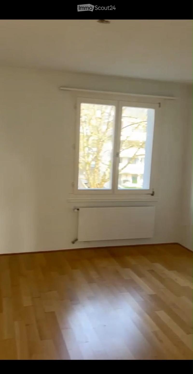 Empty room with wooden flooring, white walls, large window, and radiator under the window.