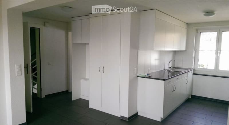 Modern kitchen with white cabinets, a sink, and a faucet. The space is clean and organized with a dark tiled floor and a window providing natural light.