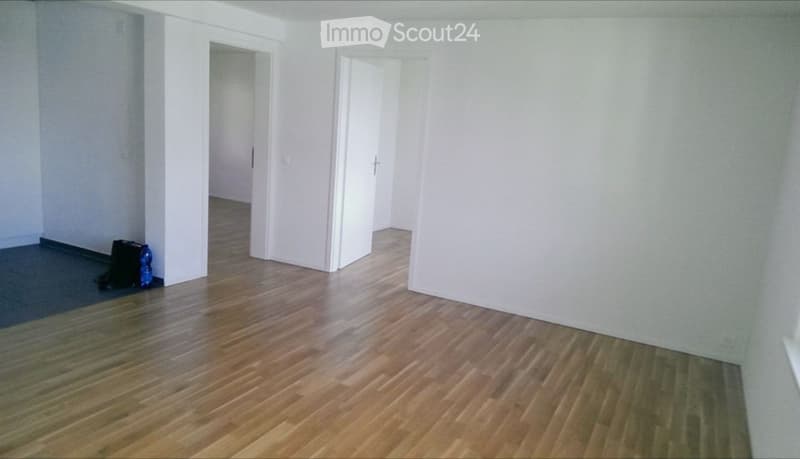 Empty room with wooden flooring, white walls, and two open doors leading to other spaces.