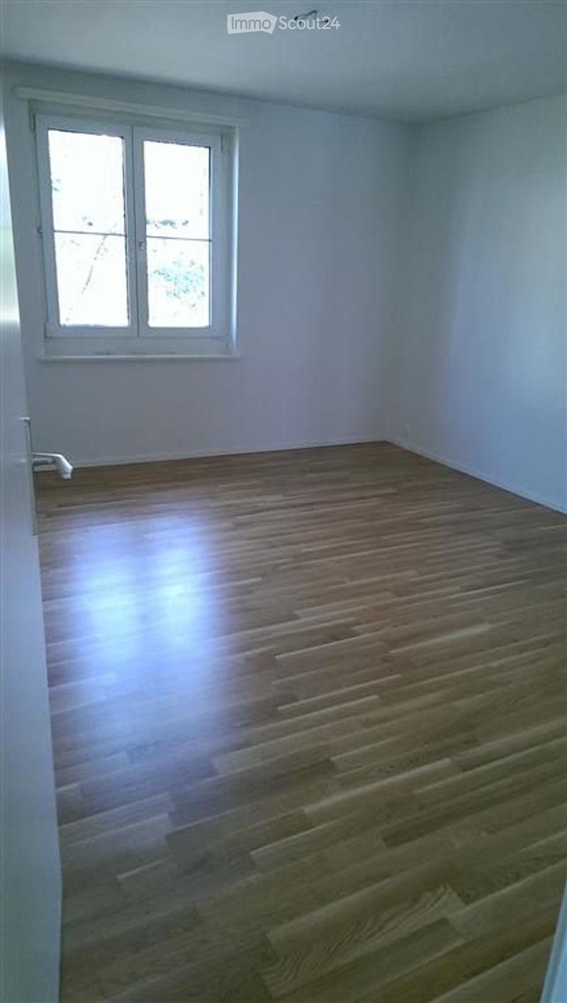 Completely empty room with wooden flooring and white walls, featuring a single window with white frame.