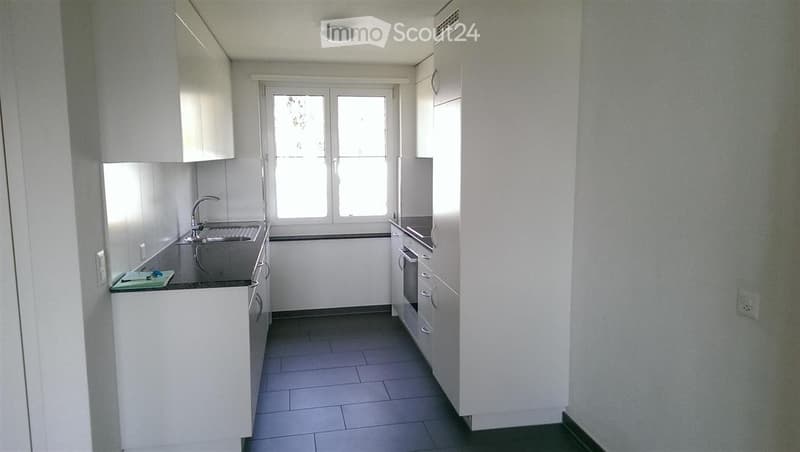 Empty kitchen with white cabinets, stainless steel sink, and tiled floor. No furniture or appliances present.