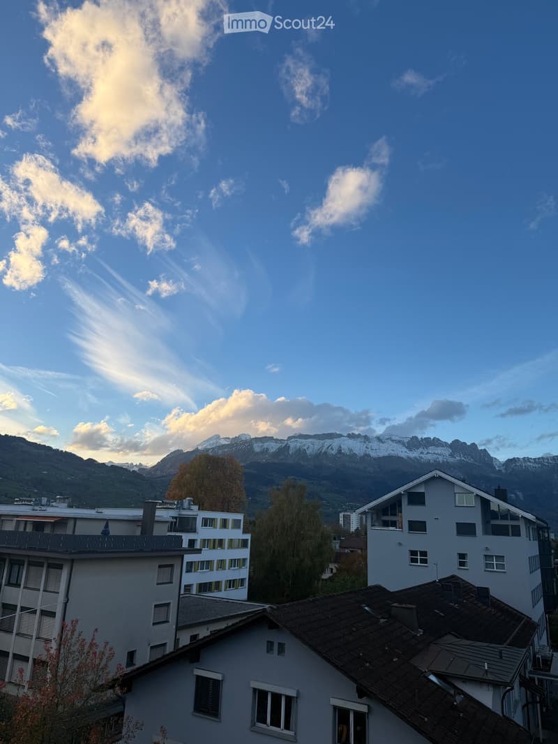 View of residential buildings with snow-capped mountains in the background under a clear blue sky.
