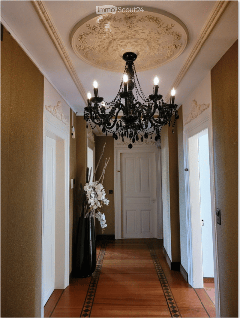 Elegant hallway with wooden flooring, ornate ceiling, chandelier, and decorative vases with white flowers.