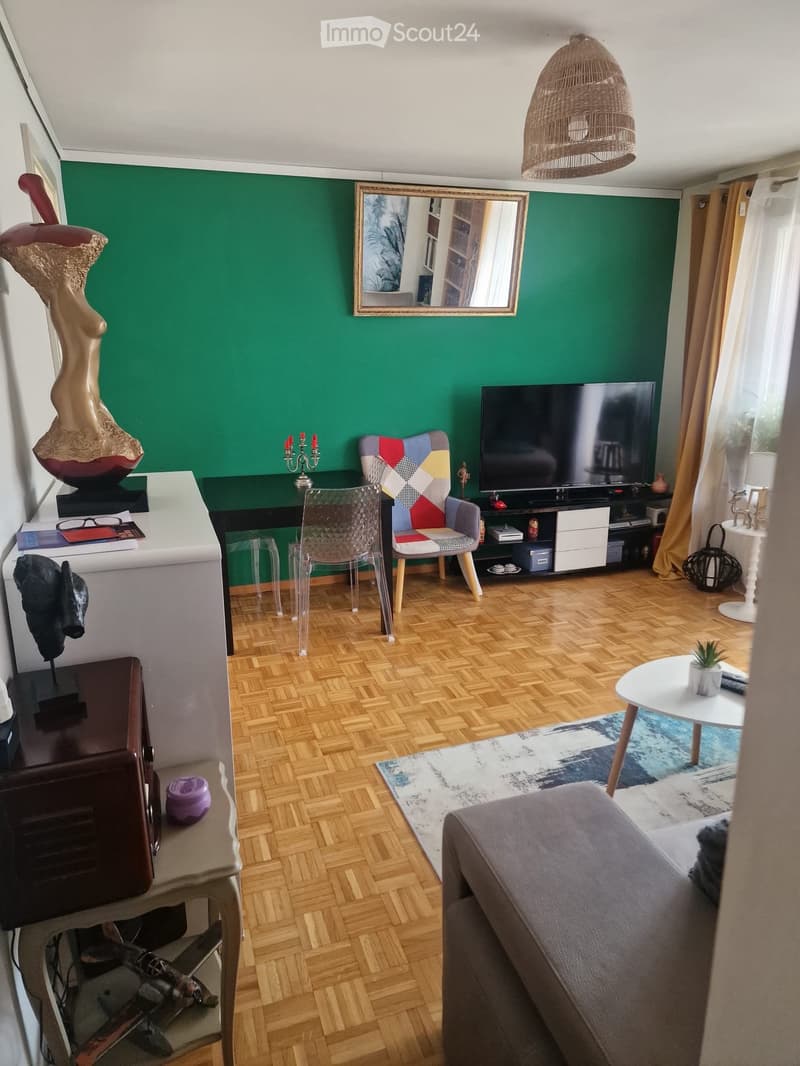 Living room with wooden flooring, green accent wall, sofa, colorful chair, TV, mirror, and decorative items.