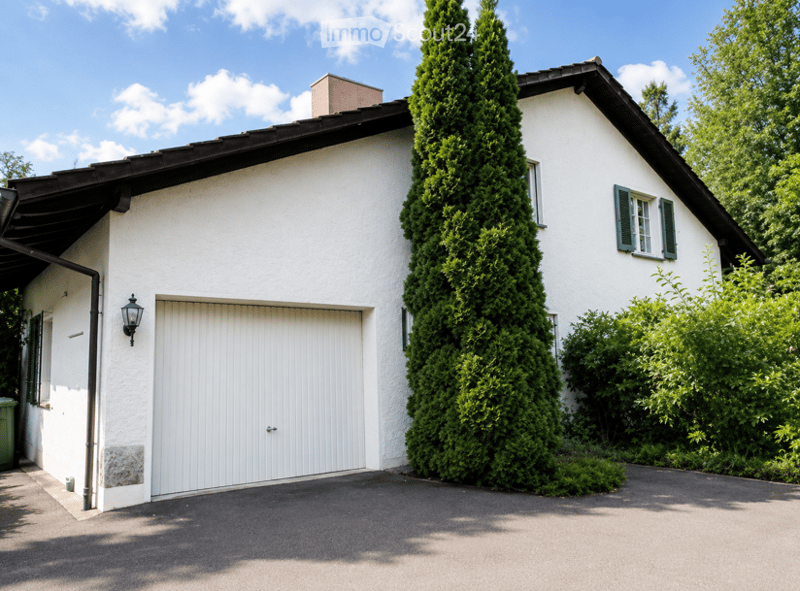 Single-story white house with a garage door, green shutters, and a tall conifer tree in front.