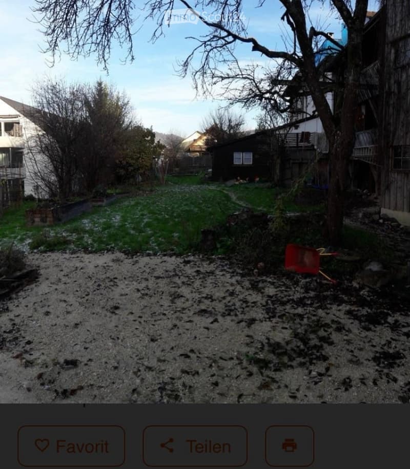 Garden area with grass, bare trees, gravel path, and a red wheelbarrow. Surrounding houses and structures are visible in the background.