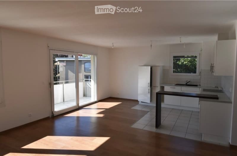 Bright, unfurnished room with wooden flooring, white cabinetry, and a large sliding glass door leading to a balcony.
