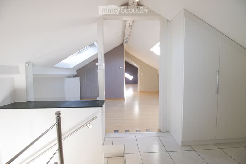Modern, minimalist hallway with white walls, wooden flooring, and skylight windows. Features a staircase with a metal railing and a small landing area.