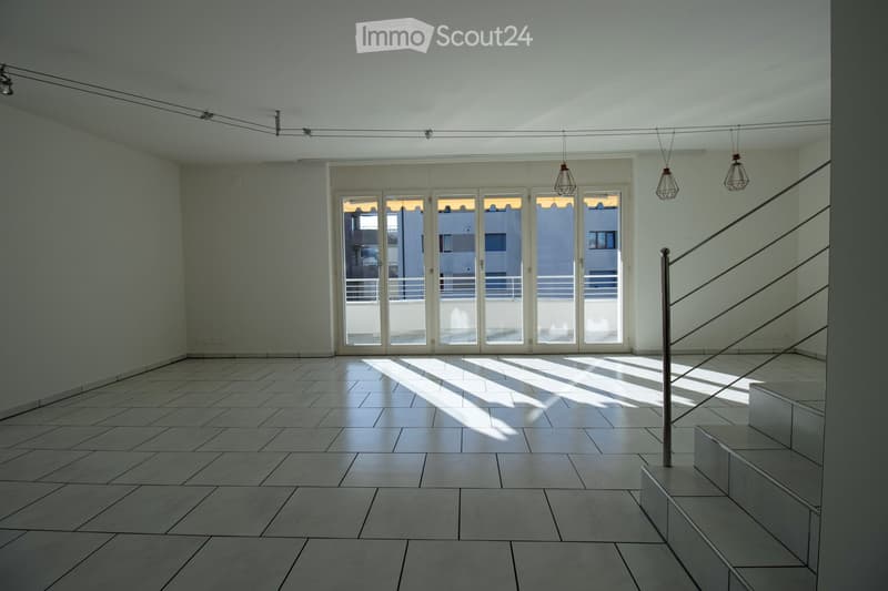 Empty room with tiled floor, white walls, large glass doors leading to a balcony, and modern pendant lights.