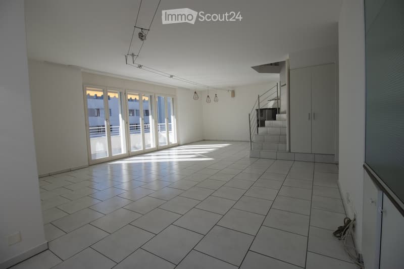 Empty room with tiled floor, white walls, large glass doors leading to a balcony, and a staircase leading to another level.