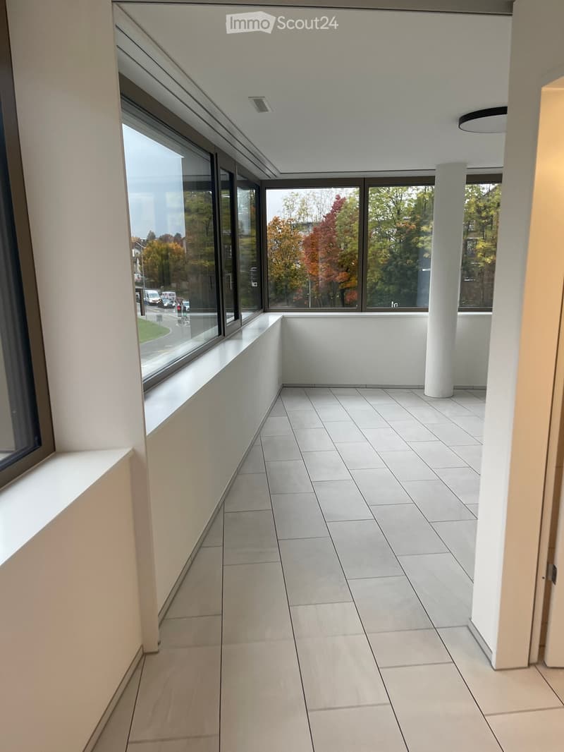 Modern hallway with large windows, white tiled floor, and a white column. The space is clean and minimalistic with natural light streaming in.